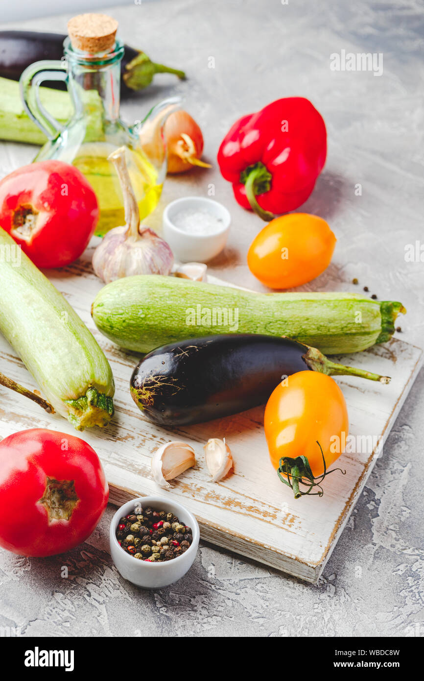 Vegetable background - wooden cutting board, tomatoes, zucchini, eggplant, onion, garlic and spices on a light background. Stock Photo