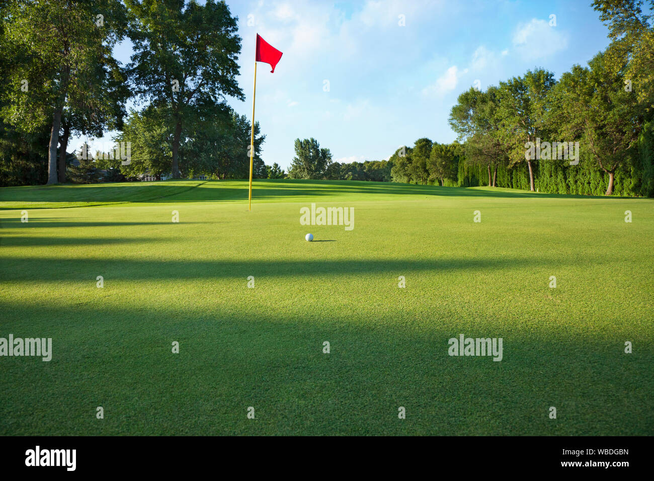 Low angle view of a golf green with red flag and ball on a sunny afternoon Stock Photo