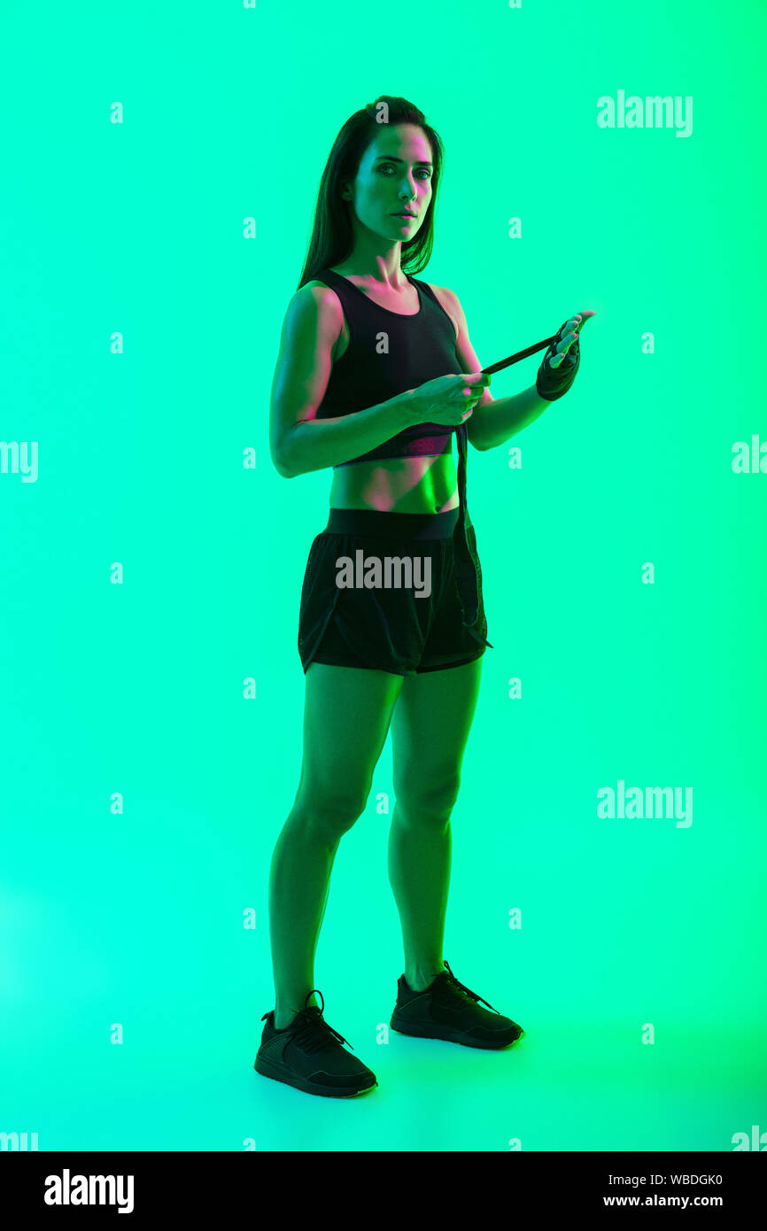 Beautiful young fitness girl standing isolated over green neon background Stock Photo