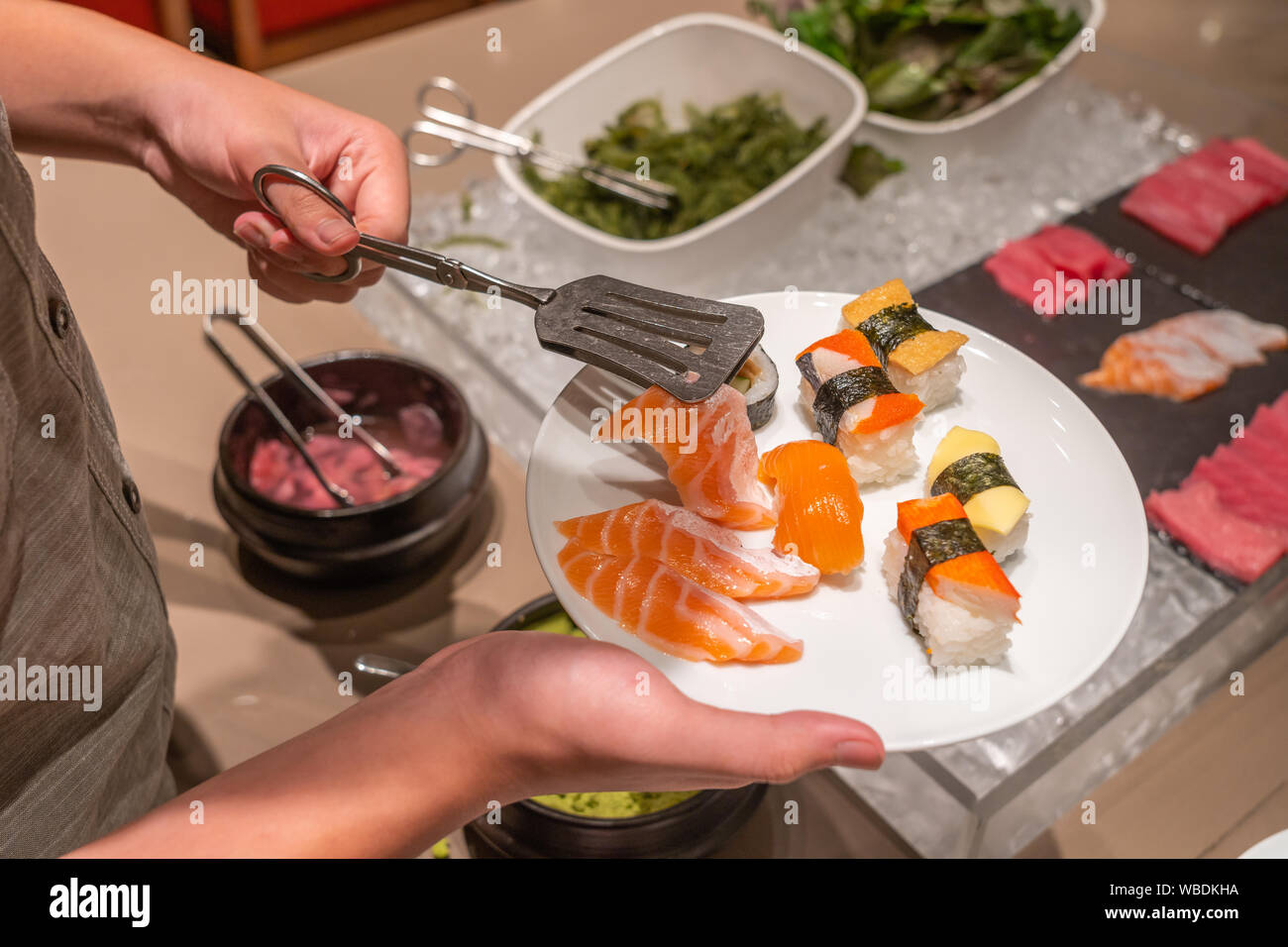 Human hand using tongs picking assorted sushi in buffet restaurant