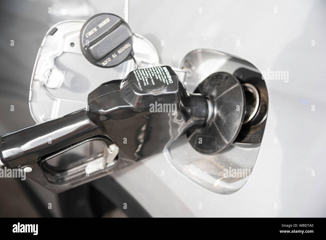 A silvercolor vehicle’s empty gas tank is being filled with fuel at the gas station Stock Photo