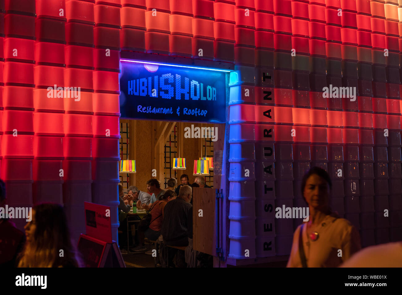 Stadtfest Brugg 24th of august 2019. night photography. Red and bluek illuminated plastic wall of Kubus Kolor with people walking in the street Stock Photo