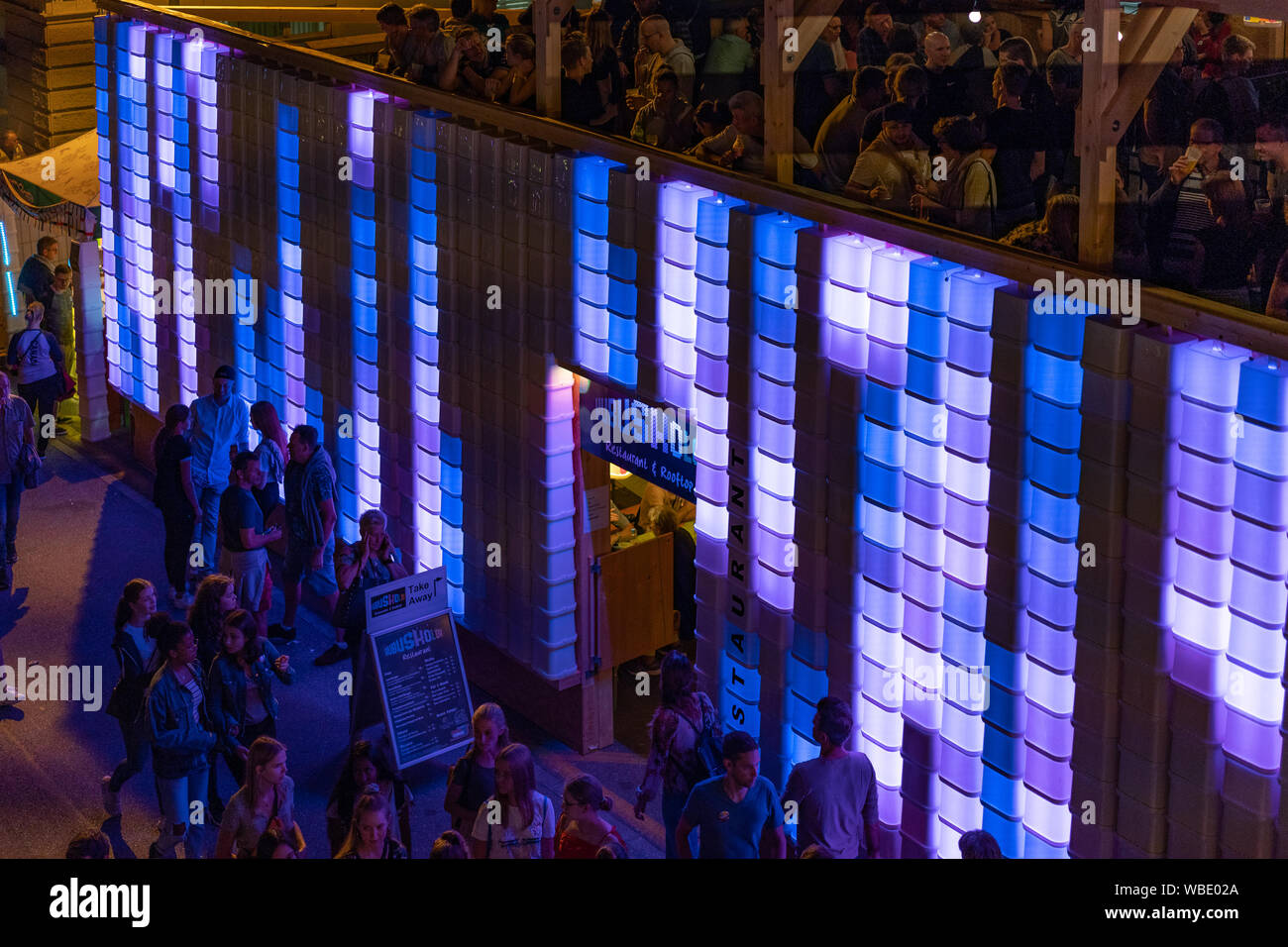 Stadtfest Brugg 24th of august 2019. street photography. Lilac and blue enlightened plastic wall of Kubus Kolor with people on the top and people walk Stock Photo