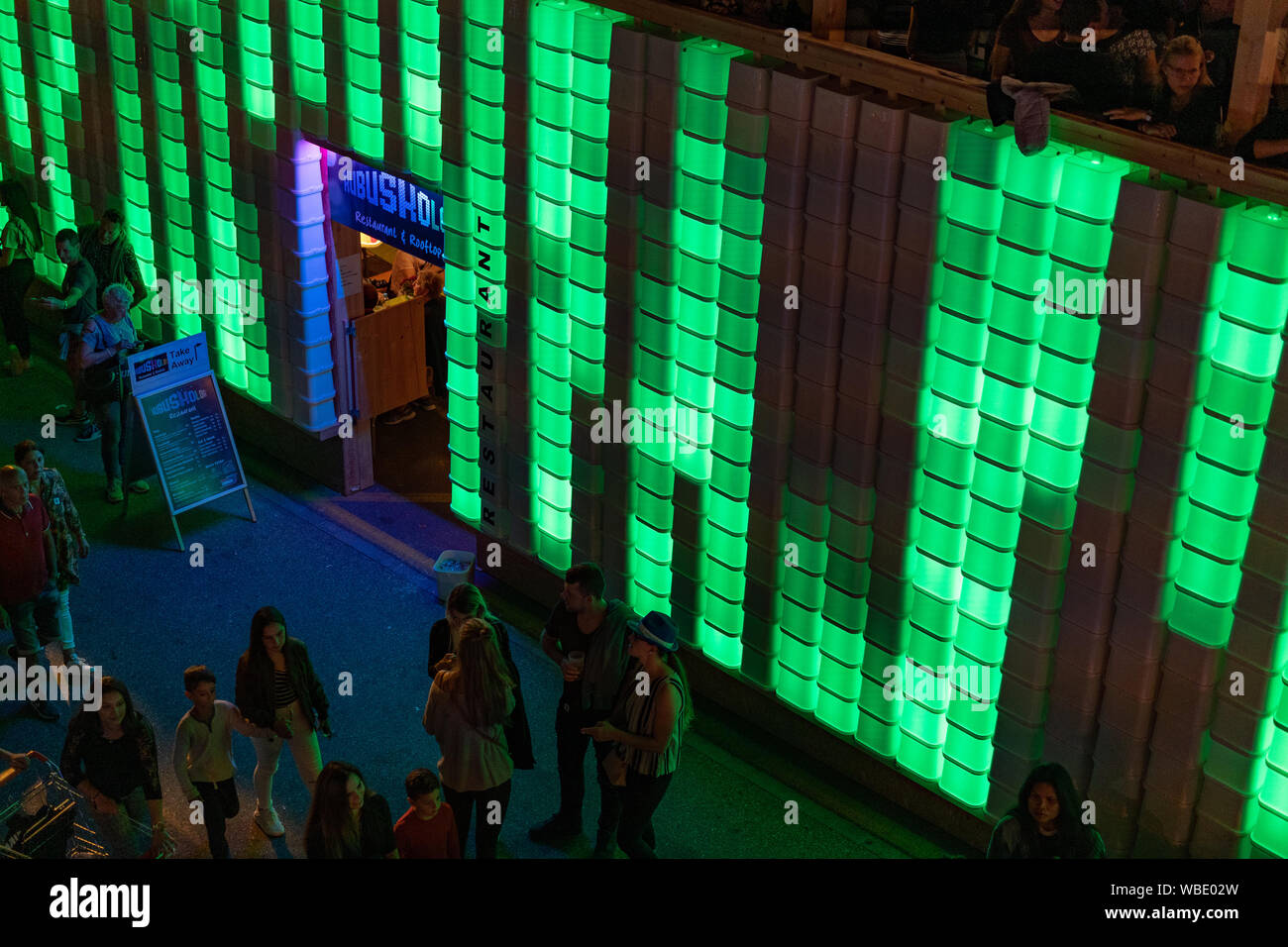 Stadtfest Brugg 24th of august 2019. night photography. Green enlightened plastic wall of Kubus Kolor with people on the top and people walking Stock Photo