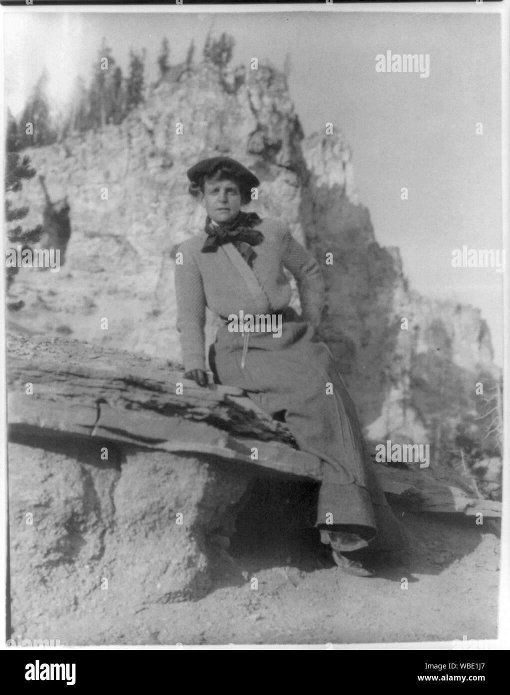 Frances Benjamin Johnston, full-length portrait, sitting on ledge with mountains in background Abstract/medium: 1 photographic print. Stock Photo