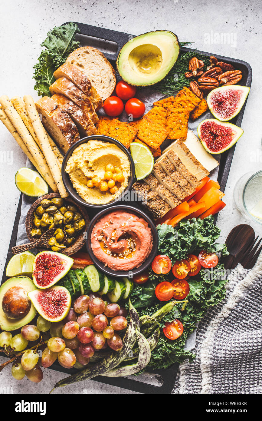 Vegan appetizer platter. Hummus, tofu, vegetables, fruits and bread on a black tray, white