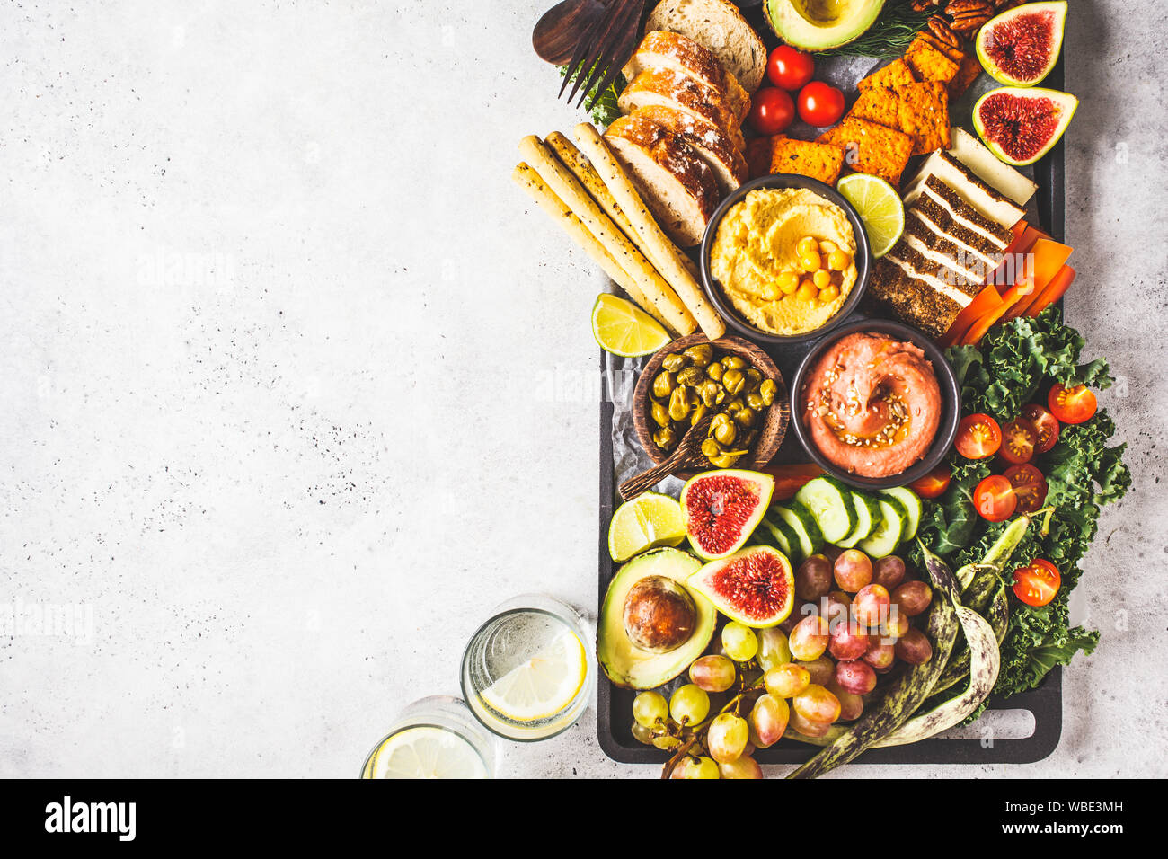 Vegan appetizer platter. Hummus, tofu, vegetables, fruits and bread on a black tray, white