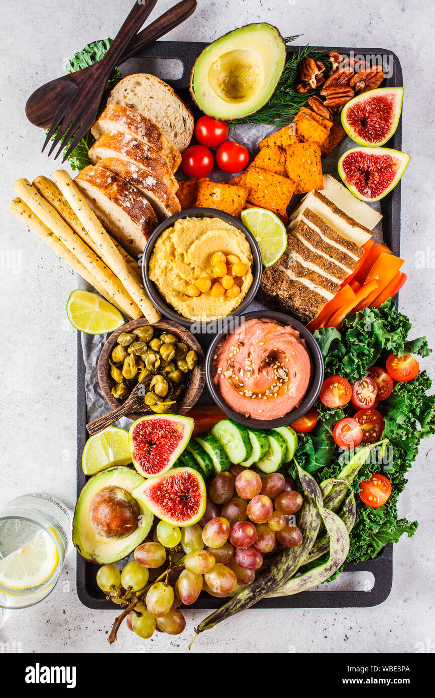 Vegan appetizer platter. Hummus, tofu, vegetables, fruits and bread on a black tray, white