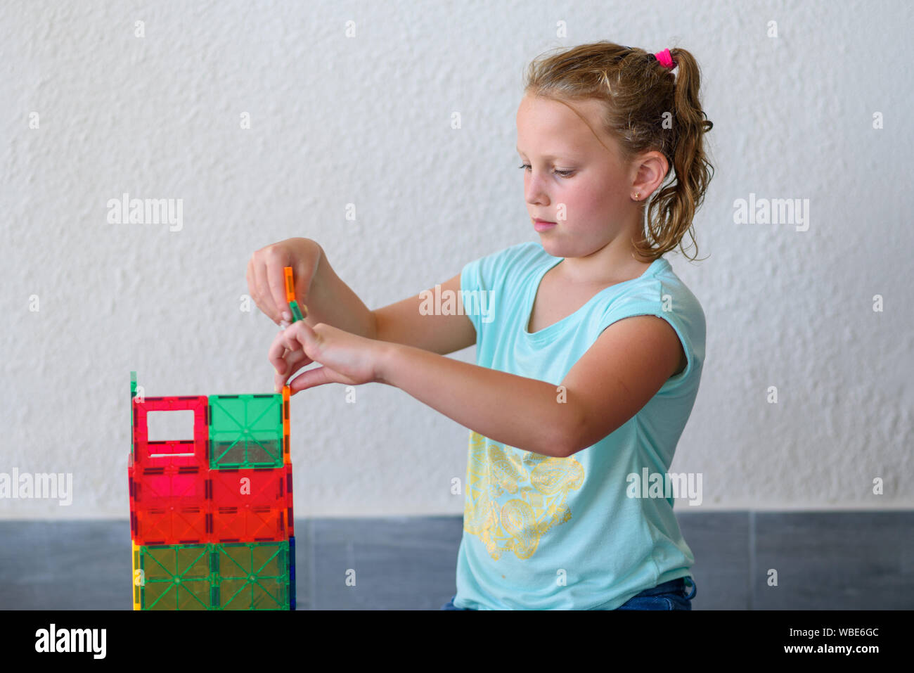 Beautiful teenage girl playing with lots of colorful plastic blocks ...