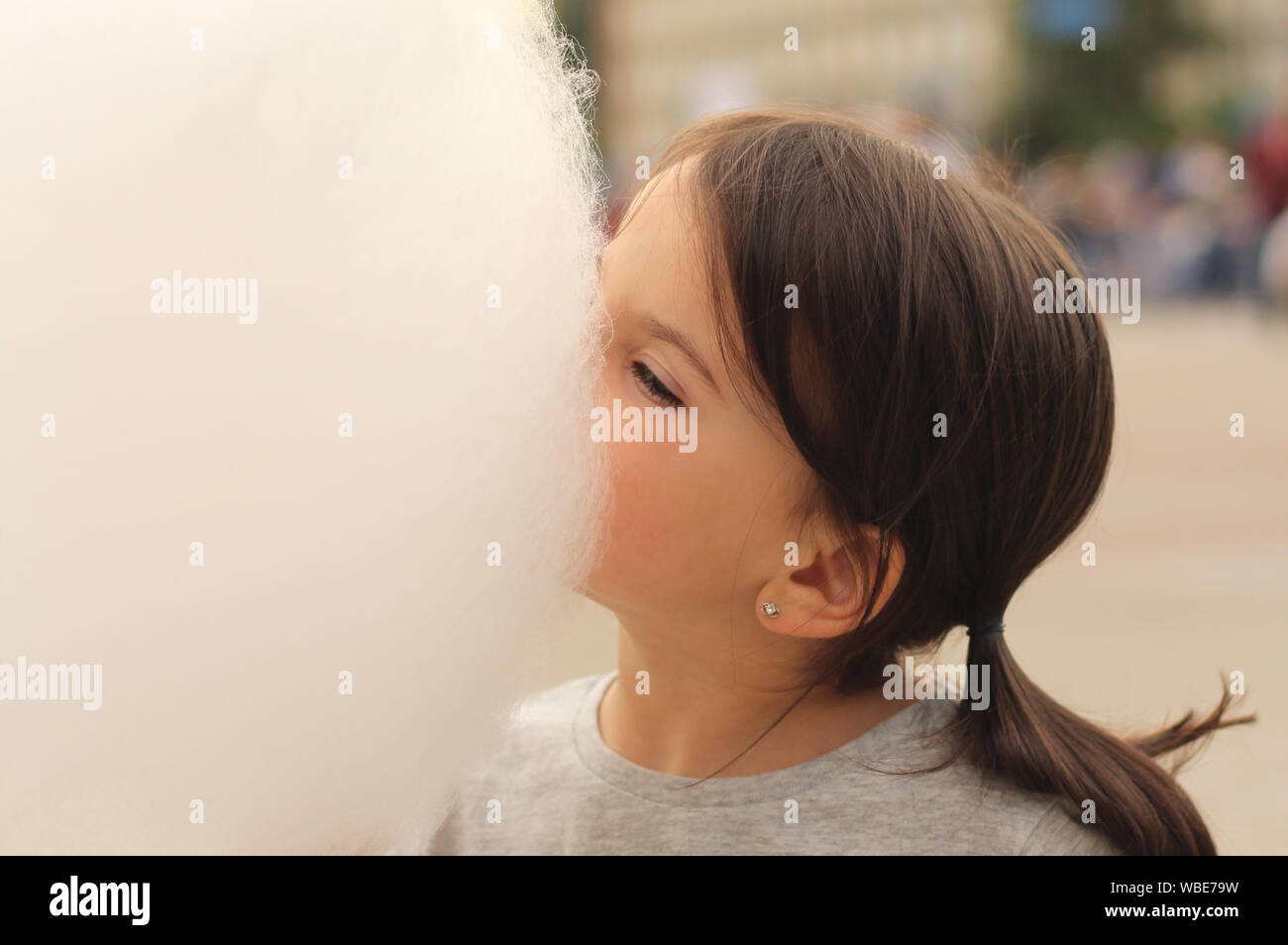 Little girl with pigtails tries to bite a big ball of cotton candy at a city celebration Stock