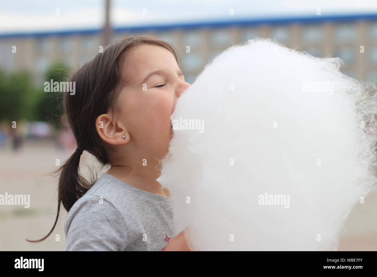 Little girl with pigtails tries to bite a big ball of cotton candy at a city celebration Stock