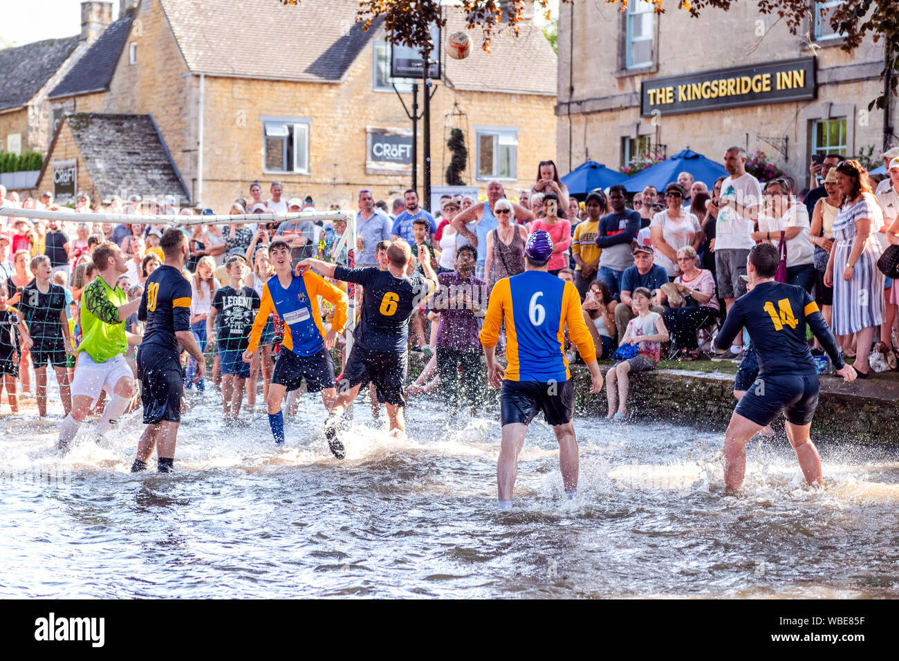Charity football match played in the River Windrush at Bourton-on-the-Water, Cotswolds, UK. Football game in river on August Bank Holiday Monday. Stock Photo