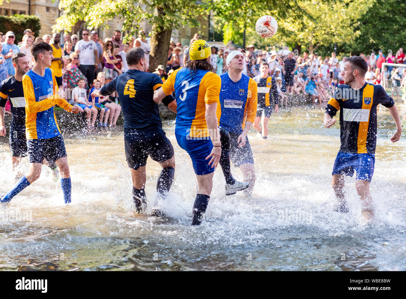 Charity football match played in the River Windrush at Bourton-on-the-Water, Cotswolds, UK. Football game in river on August Bank Holiday Monday. Stock Photo