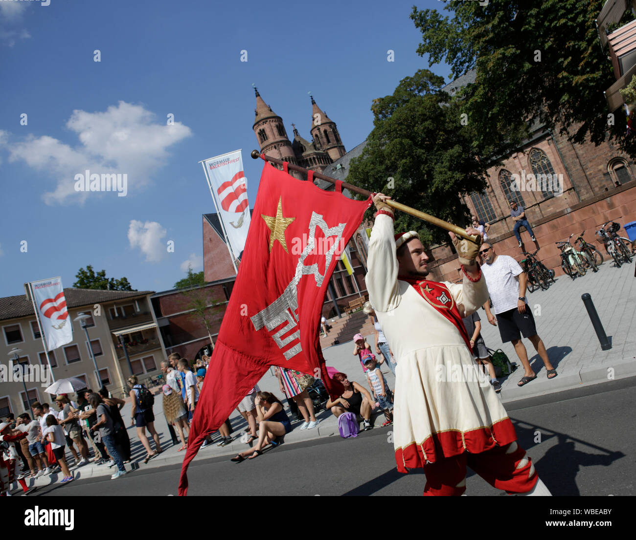 Worms, Germany. 25th August 2019. A colour guard of the journeymen marches in the parade, carrying a flag with the coat of arms of Worms. The first highlight of the 2019 Backfischfest was the big parade through the city of Worms with over 70 groups and floats. Community groups, music groups and businesses from Worms and further afield took part. Stock Photo