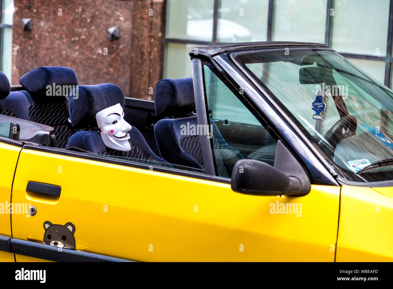 Yellow cabriolet car parked on the street with a V for Vendetta mask attached to the seat, Warsaw, Poland Stock Photo