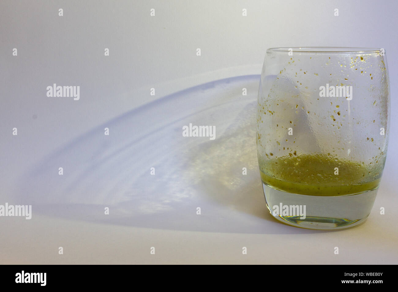 An almost empty glass of vegetable juice on a neutral pale background, casting its shadow. Includes space for copy Stock Photo