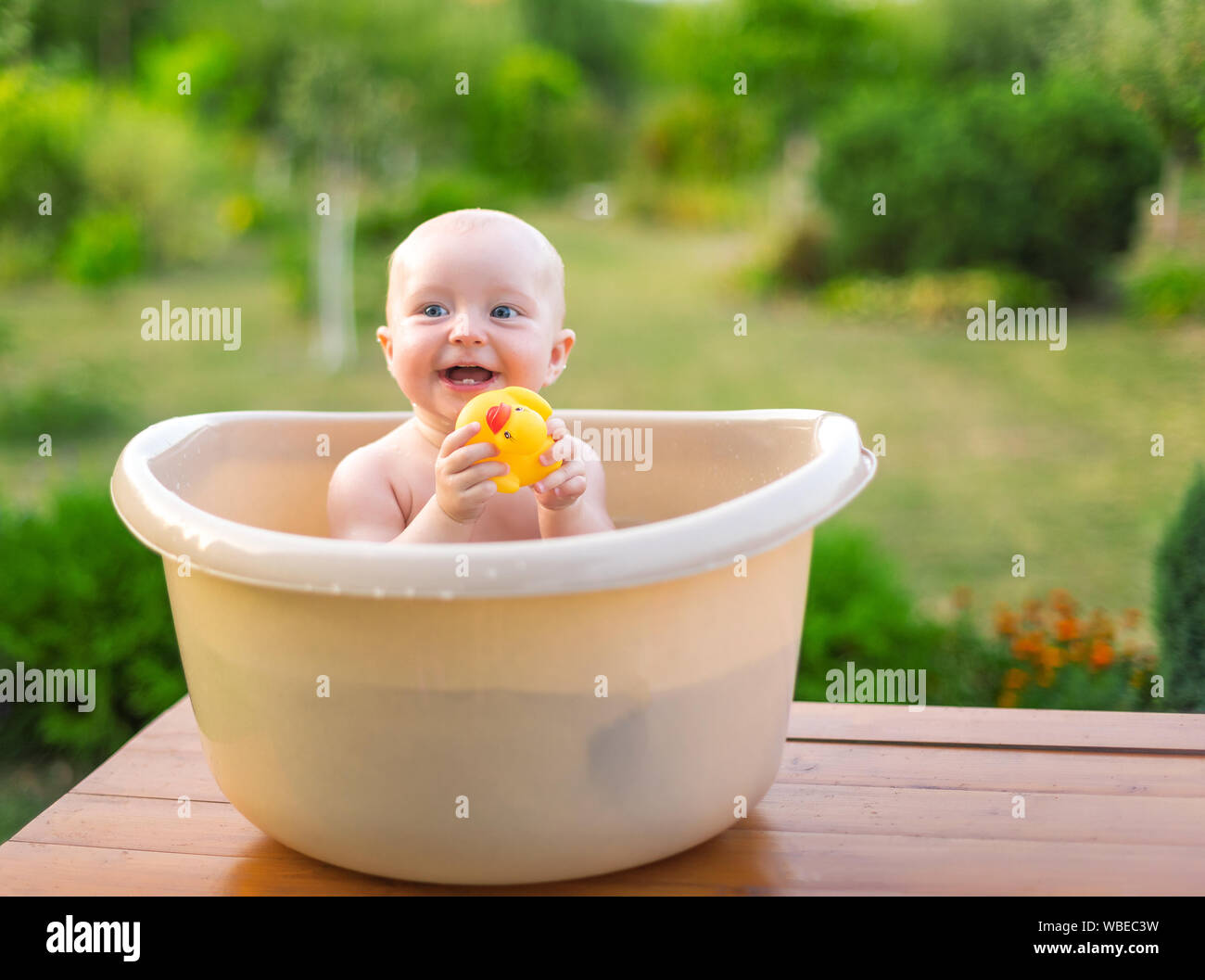 The baby bathes in a bath in the garden on a summer evening Stock Photo