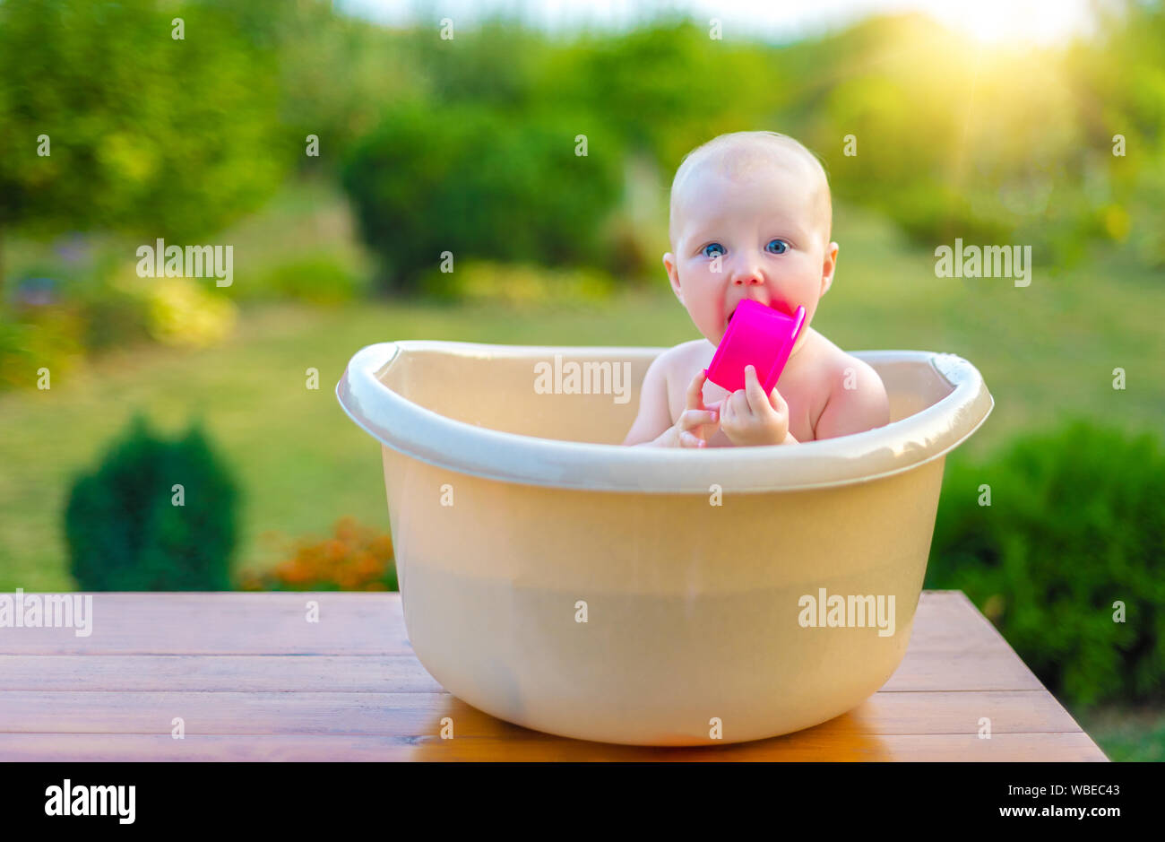 The baby bathes in a bath in the garden on a summer evening Stock Photo