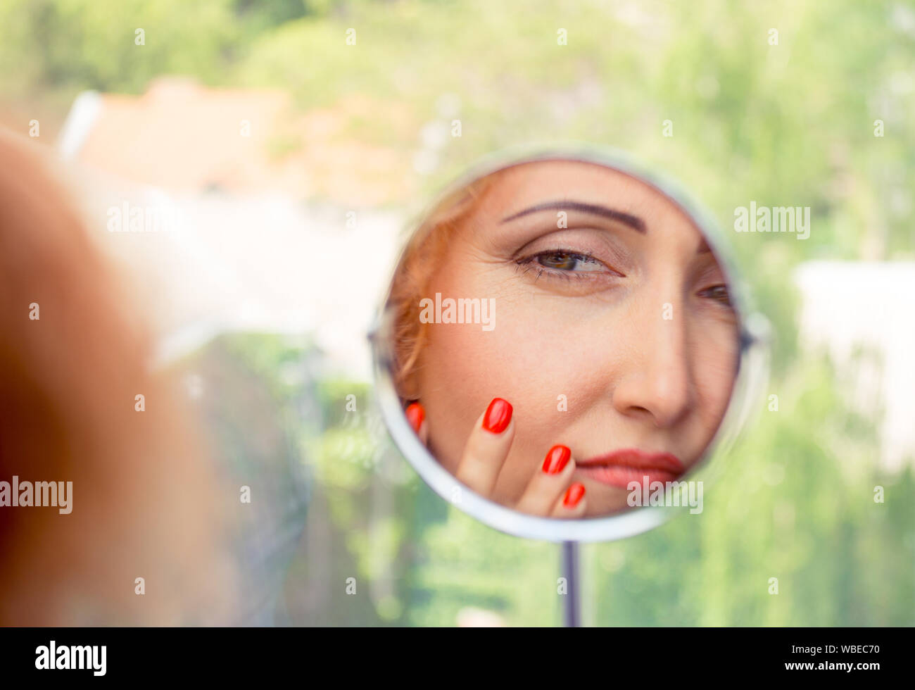 Woman looking, examining her nasolabial fold, her first signs of aging. Beauty and skincare concept of a mature woman. Stock Photo