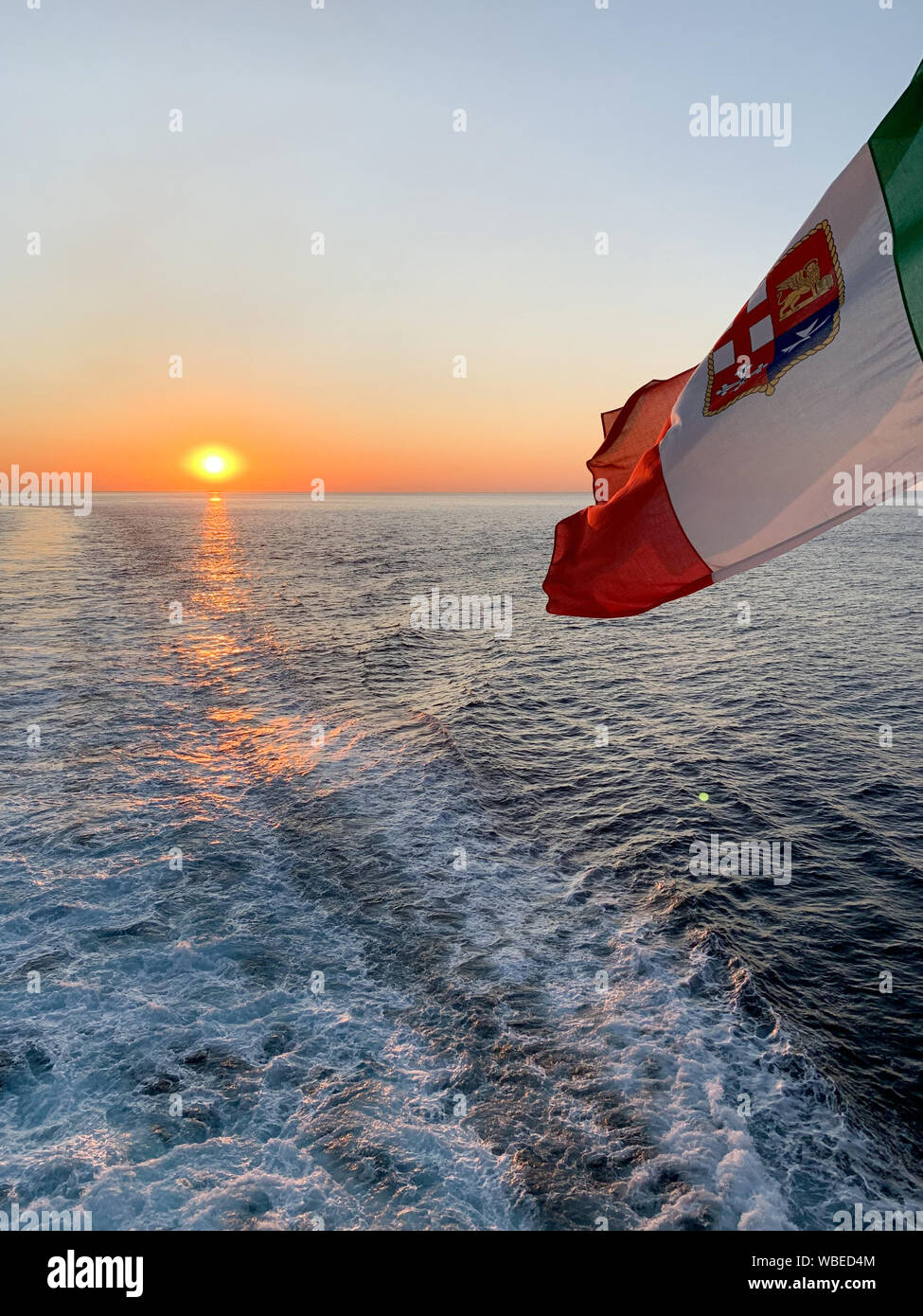 Italian flag waving on a ship sailing at sunset. Stock Photo