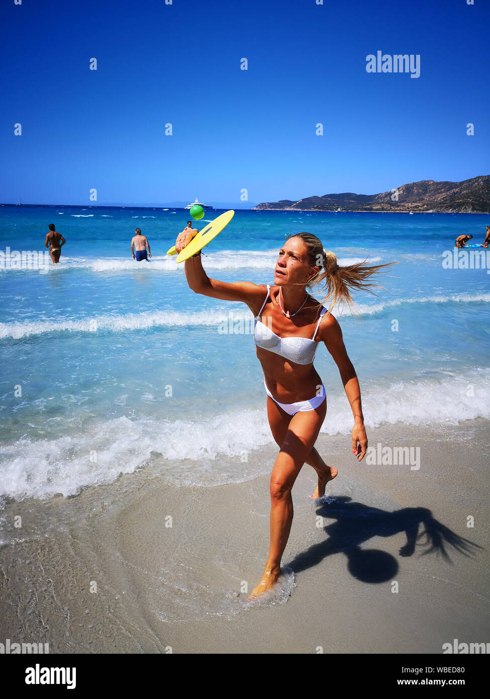 Villasimius, Italy - August 16, 2019: Woman plays beach tennis on the shore of the blue Sardinian sea. Stock Photo