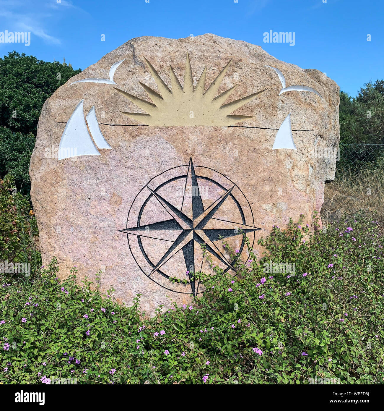 Wind rose painted on a rock surrounded by green bushes. Stock Photo