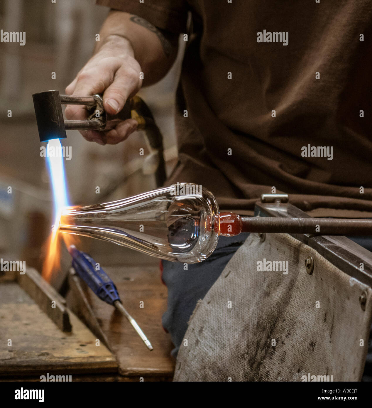 A glass blowing artist forms a blob of glass into a vessel using a
