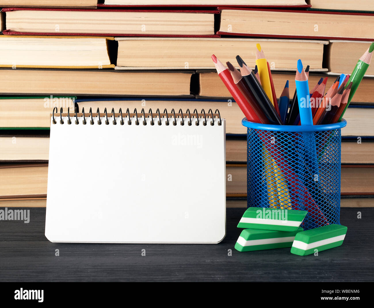 https://c8.alamy.com/comp/WBENM6/stacks-of-various-hardback-books-and-blue-stationery-glass-with-multi-colored-wooden-pencils-open-spiral-notebook-back-to-school-concept-WBENM6.jpg