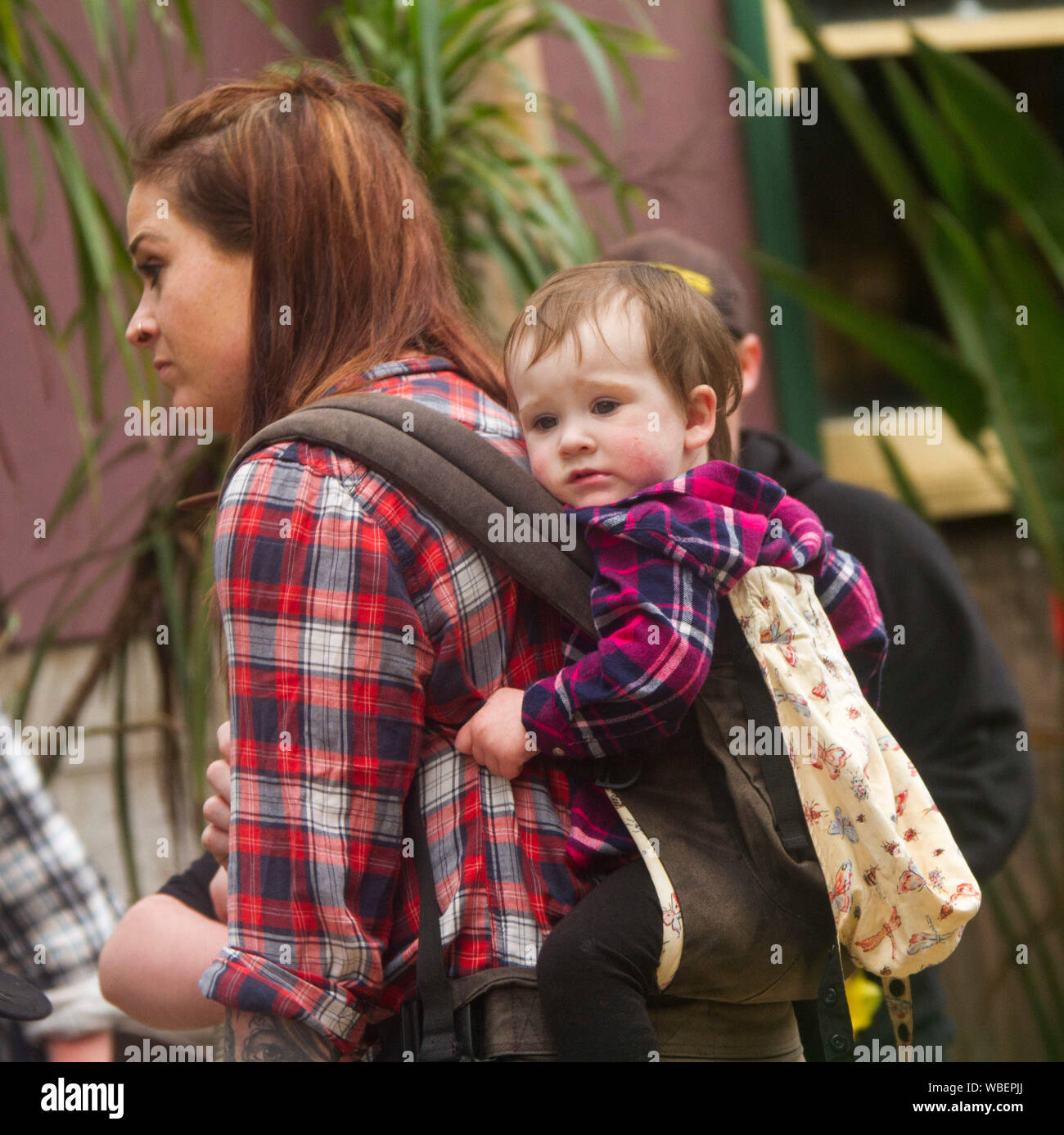 Young woman wearing bright red chequered shirt carrying baby on her back  - in NSW Australia Stock Photo