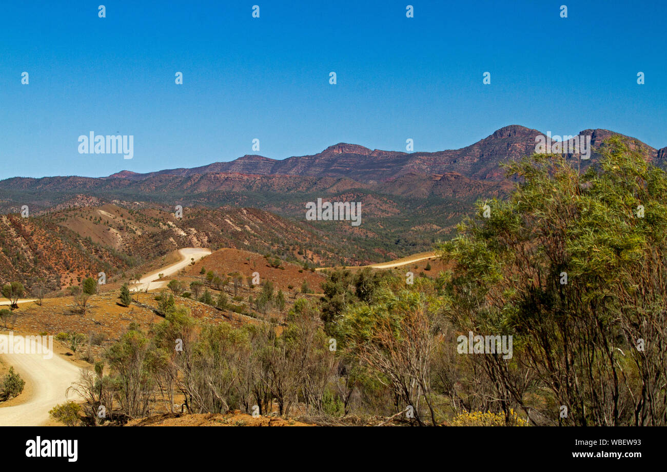 Road winding through Flinders Ranges National Park with rugged rocky ranges reaching up into blue sky, South Australia Stock Photo