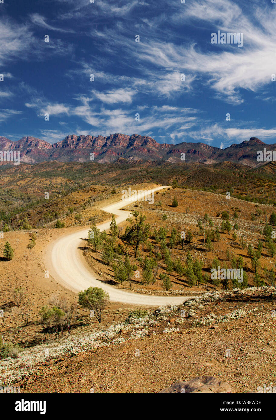 Road winding through Flinders Ranges National Park with rugged rocky ranges reaching up into blue sky streaked with clouds, South Australia Stock Photo
