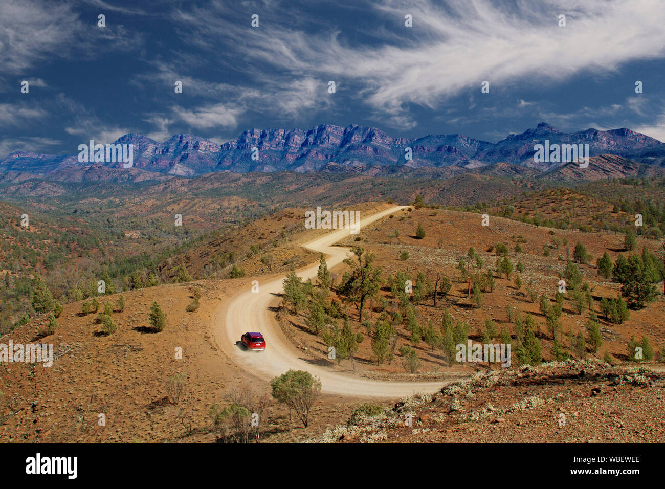 Road winding through Flinders Ranges National Park with rugged rocky ranges reaching up into blue sky streaked with clouds, South Australia Stock Photo