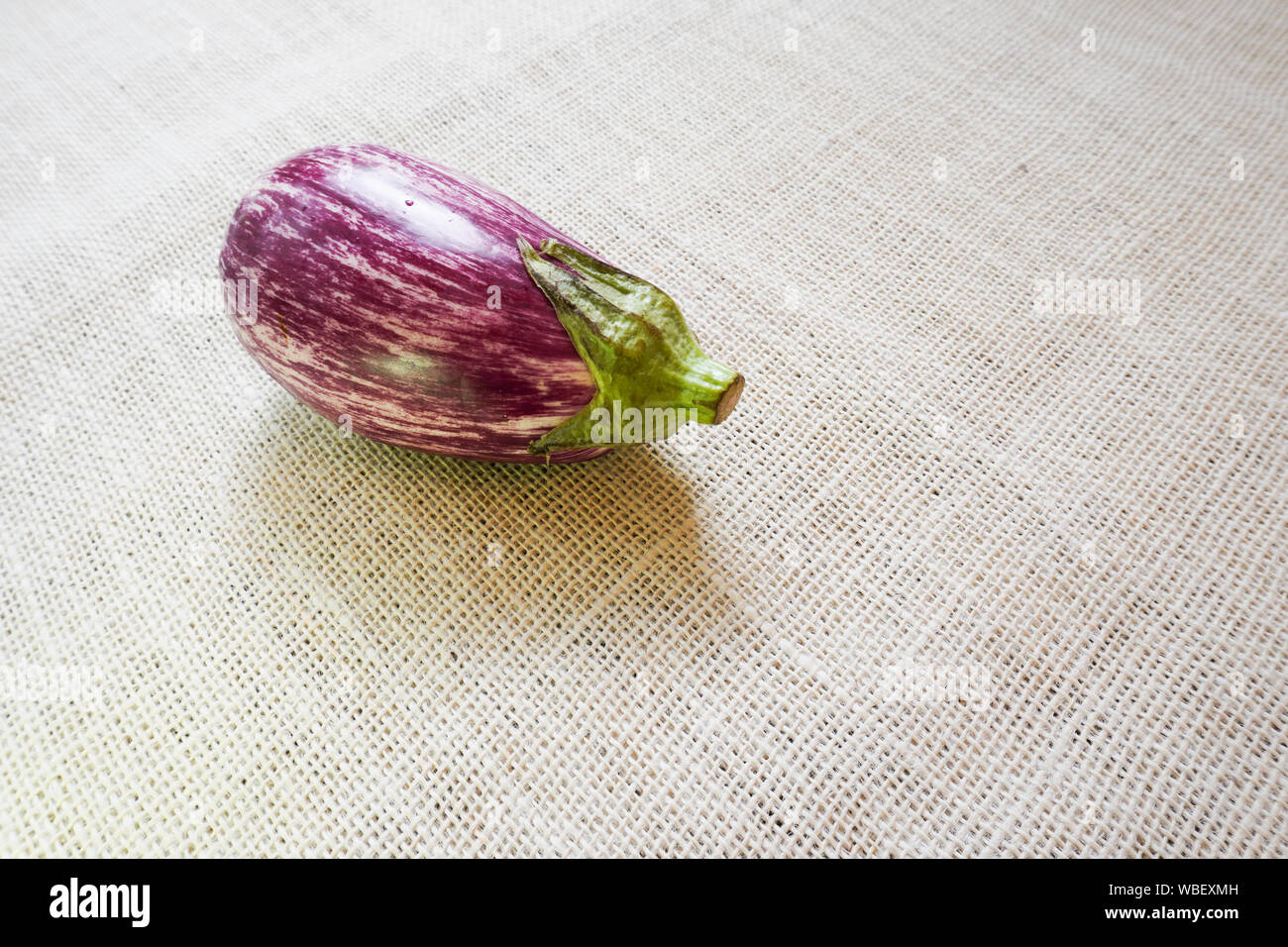 A ripe eggplant sits on a rustic burlap tablecloth Stock Photo