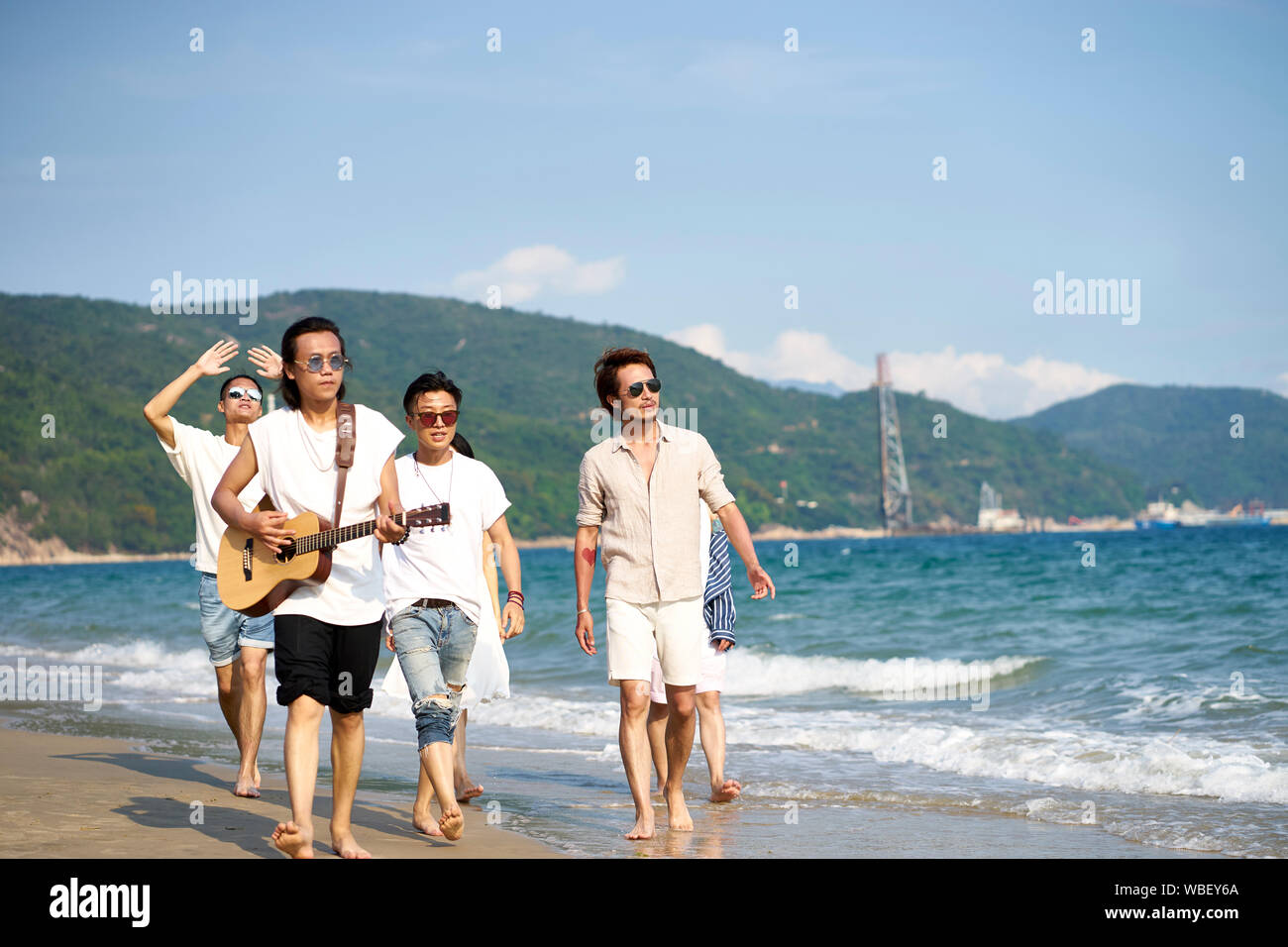 group of young asian adults men walking on beach playing guitar Stock Photo