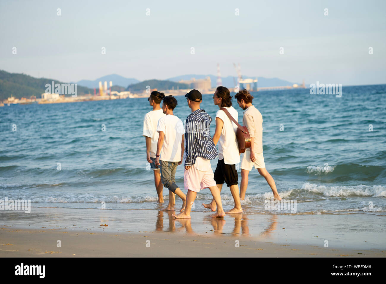group of five young asian men walking in sea water on beach Stock Photo