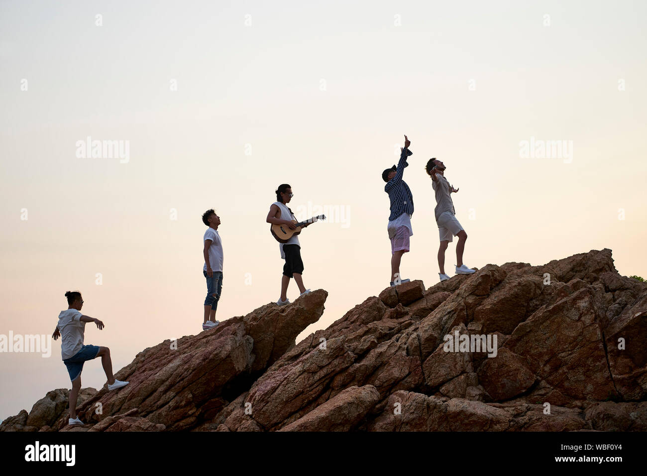 members of a rock band standing on top of rocks by the sea singing playing guitar Stock Photo