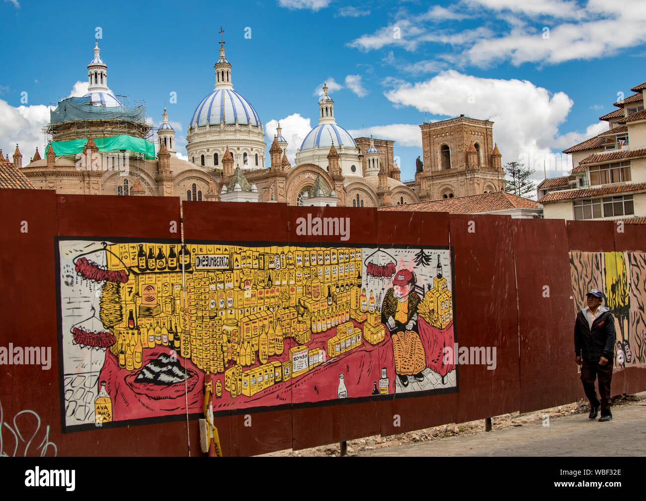Cuenca, Ecuador, Dec 24, 2017 - Man walks past construction barrier with mural painted, and Cathedral domes in the background Stock Photo
