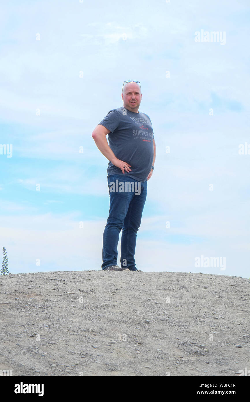 Forty something year old man standing tall on a hill with the blue sky and clouds in the background Stock Photo