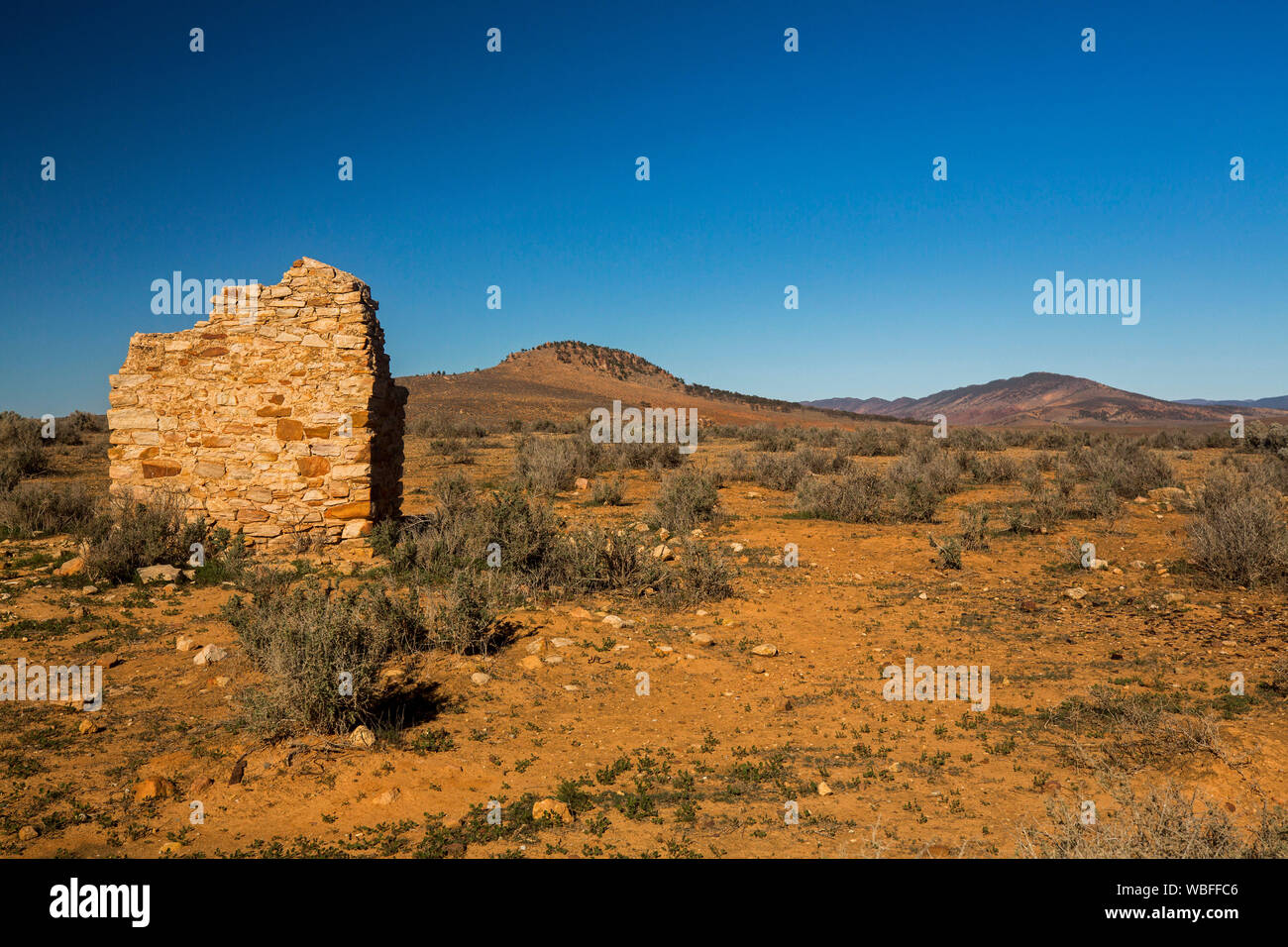 Outback landscape with ruins of Simonston on red stony soil & barren hill rising to blue sky in Flinders Ranges region north of Quorn South Australia Stock Photo