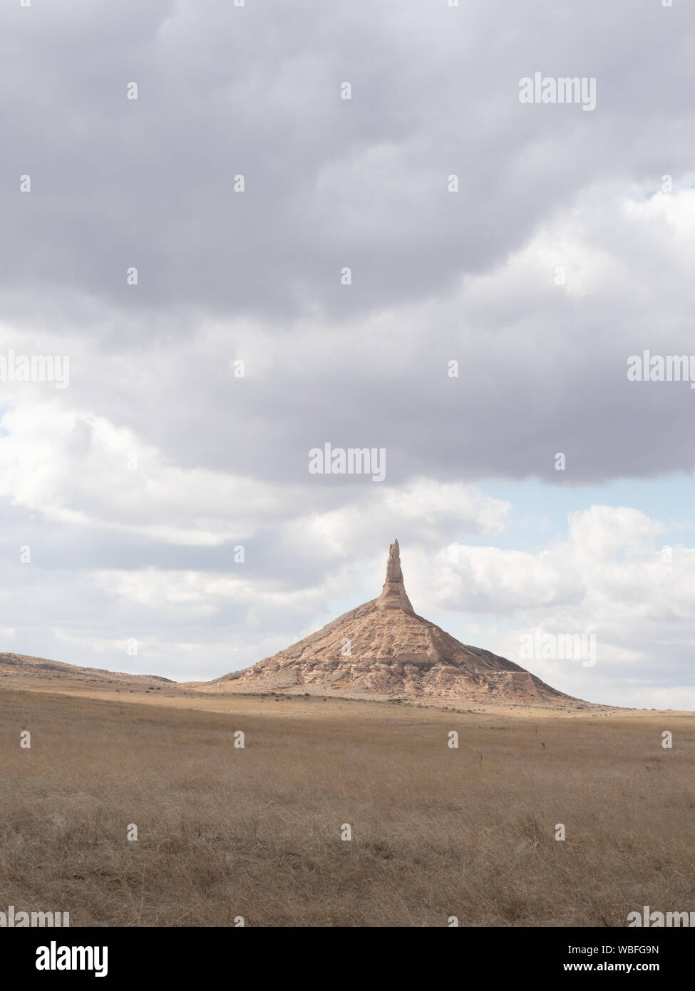 Chimney Rock National Historic Site in Nebraska with field in the foreground and cloudy skies above. Stock Photo