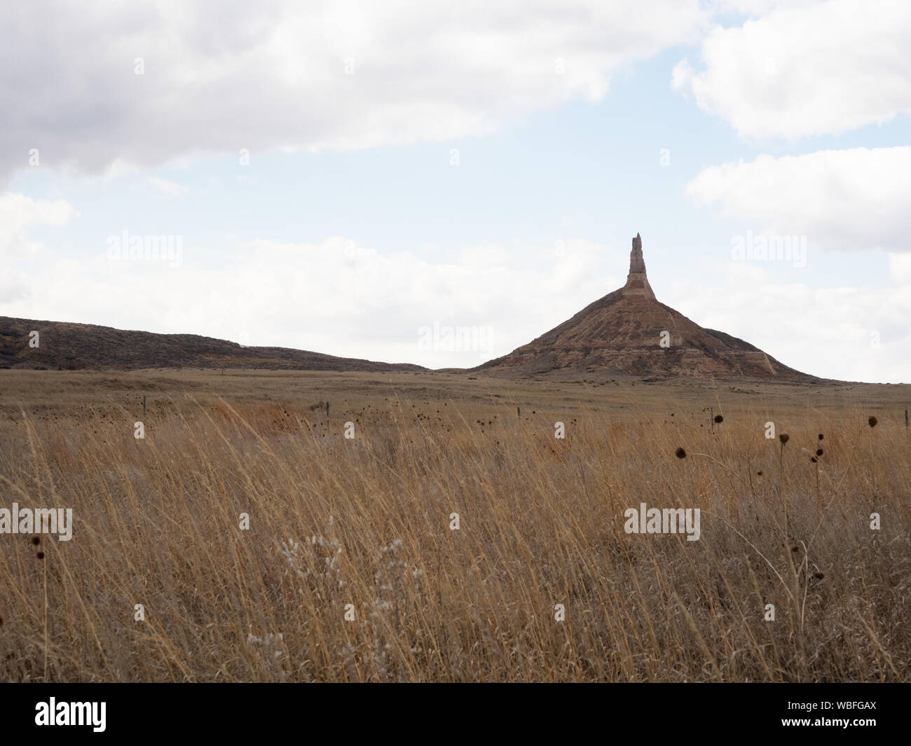 Chimney Rock National Historic Site in Nebraska with field with dried vegetation in the foreground. Cloudy skies above. Stock Photo