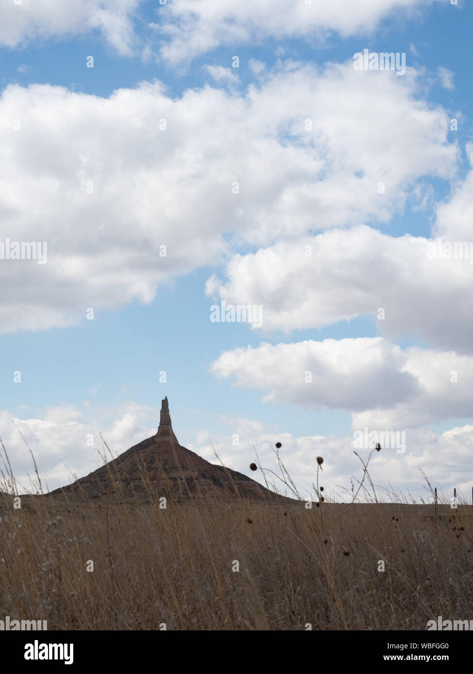 Chimney Rock National Historic Site in Nebraska with field with dried vegetation in the foreground. Cloudy skies above. Stock Photo