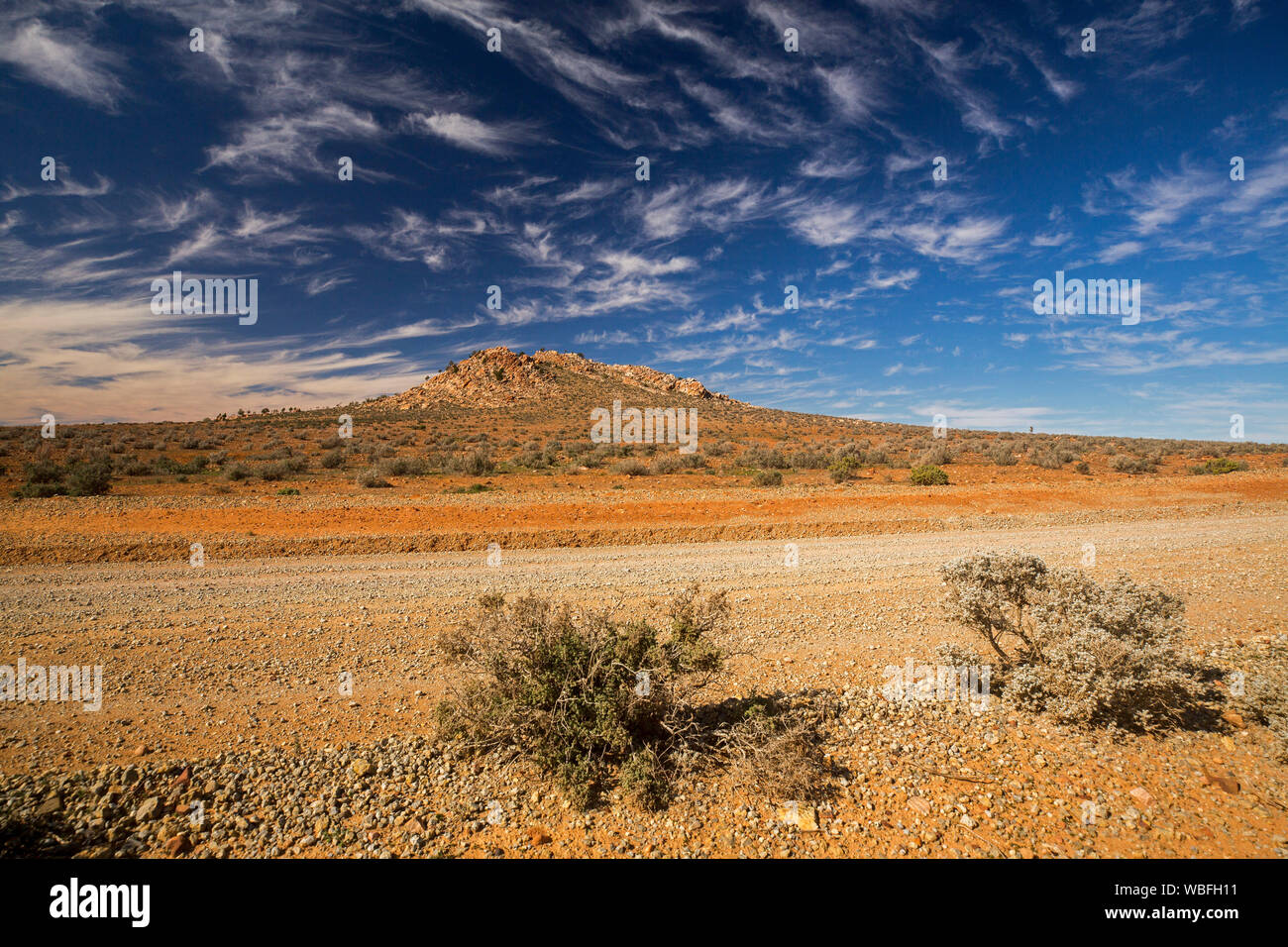 Arid stony outback landscape of Flinders Ranges region with low hill on horizon rising into blue sky freckled with clouds in South Australia Stock Photo