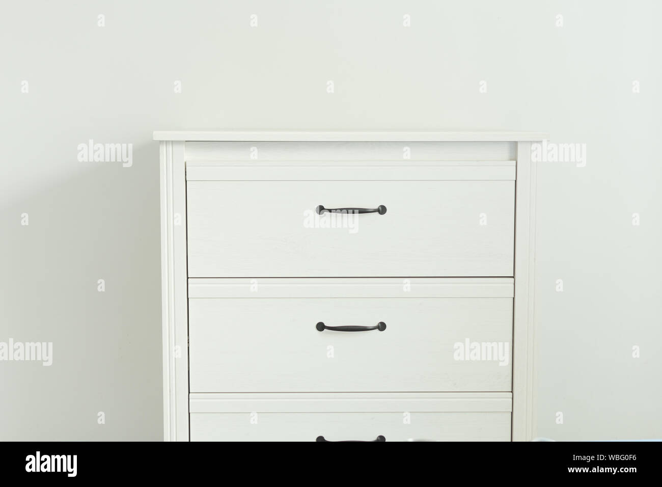 White modern chest of drawers near white wall. Furniture with drawers in a frame. Stock Photo