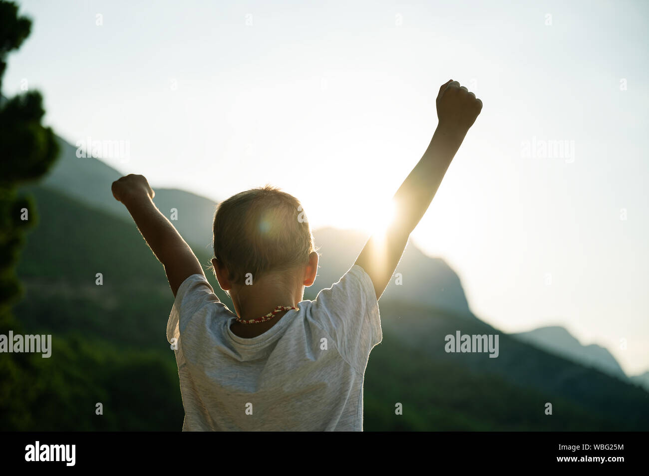 View from behind of a young child with his arms raised high in the air ...