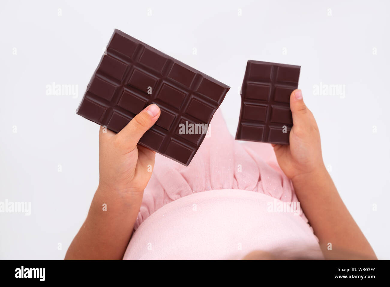 Beautiful little girl taste chocolate like a pro - breaking cacao bar. Stock Photo