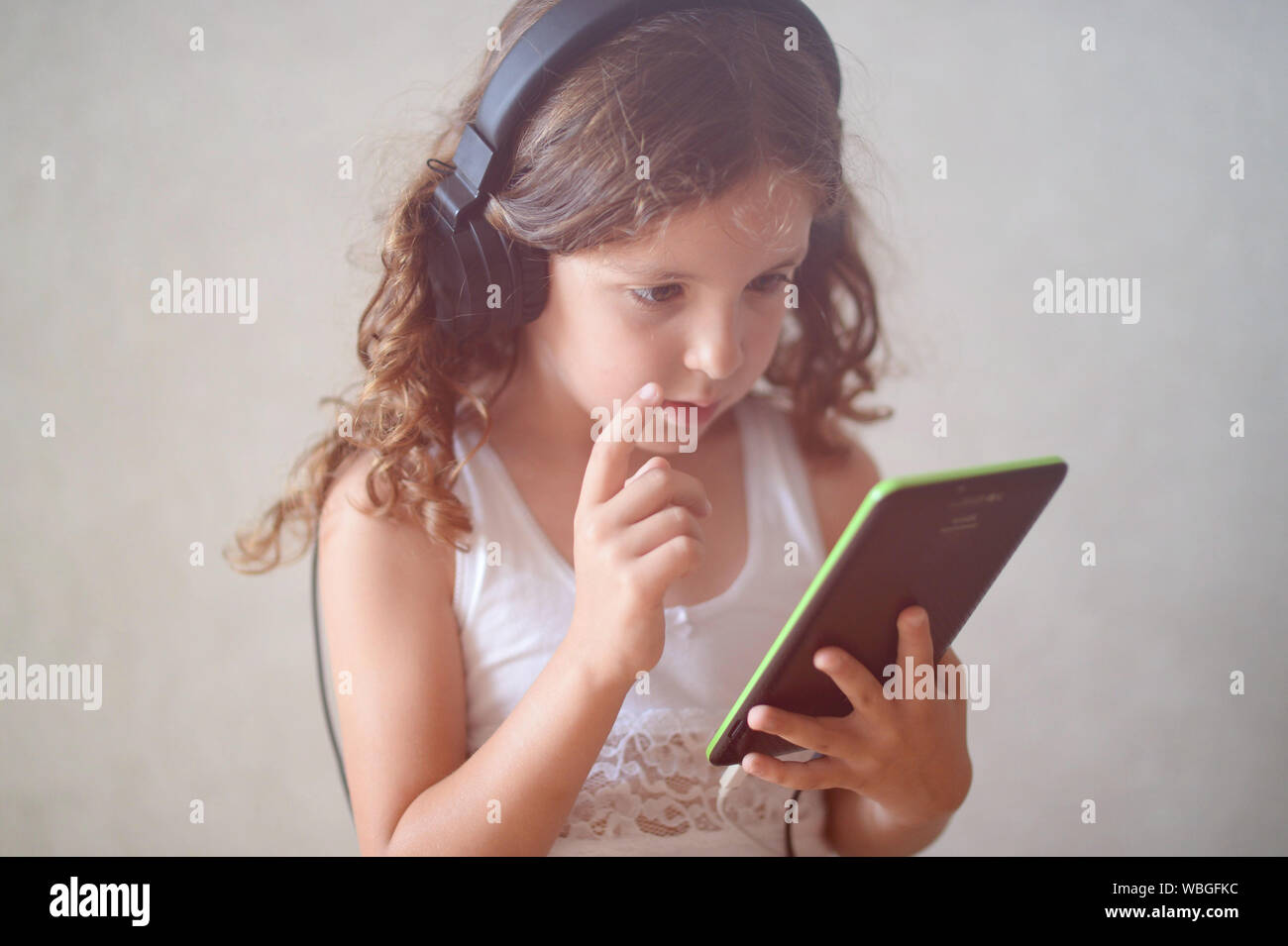 pensive caucasian little girl in earpieces holding black tablet pad Stock Photo