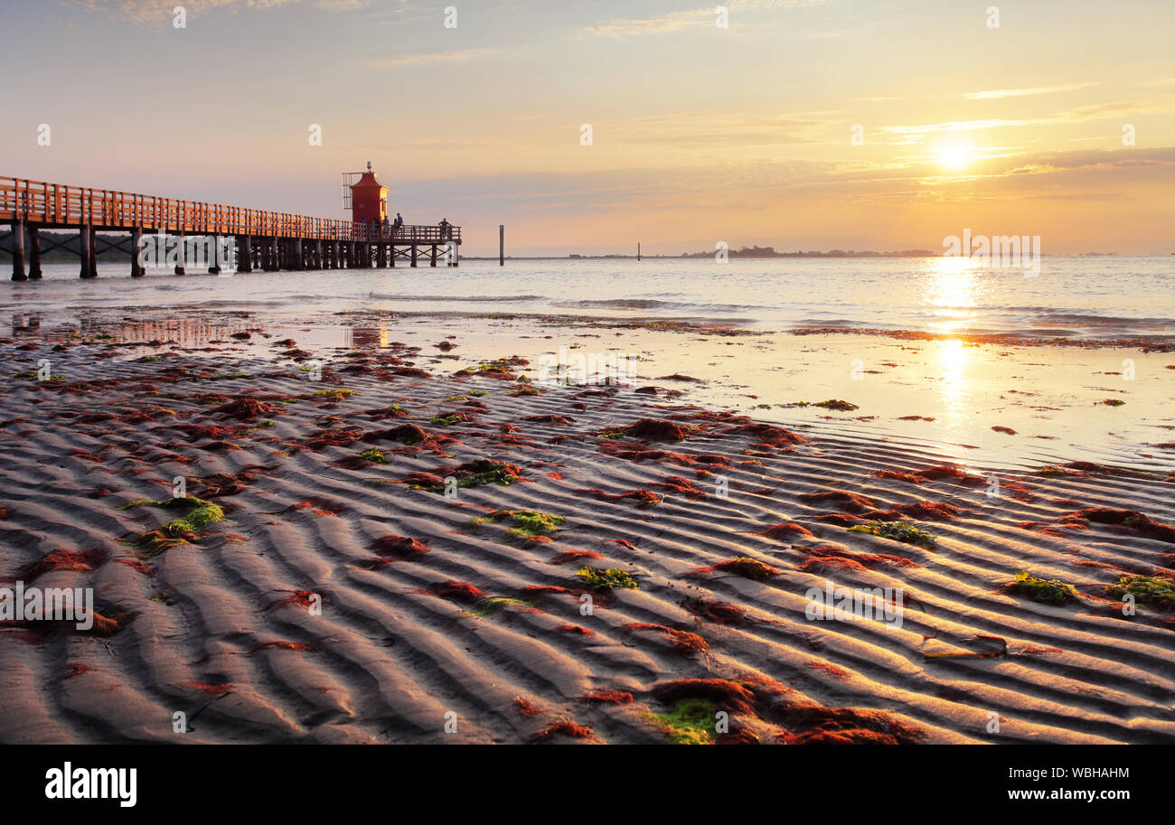 Sunrise with sun on beach with lighthouse in Italy - Lignano Stock Photo