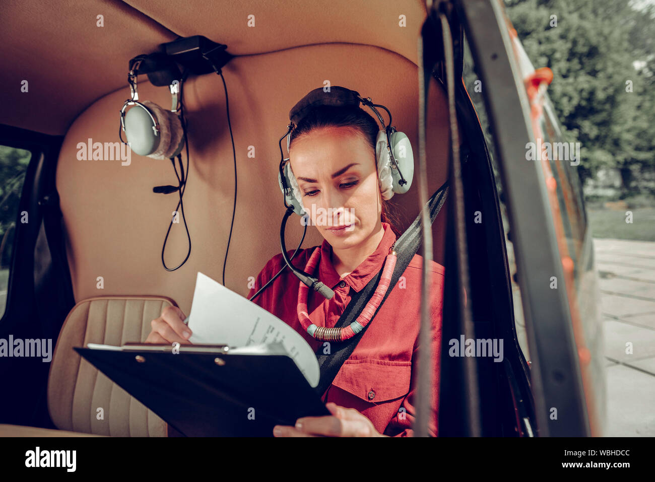 Female pilot wearing red shirt checking the documents in the helicopter Stock Photo