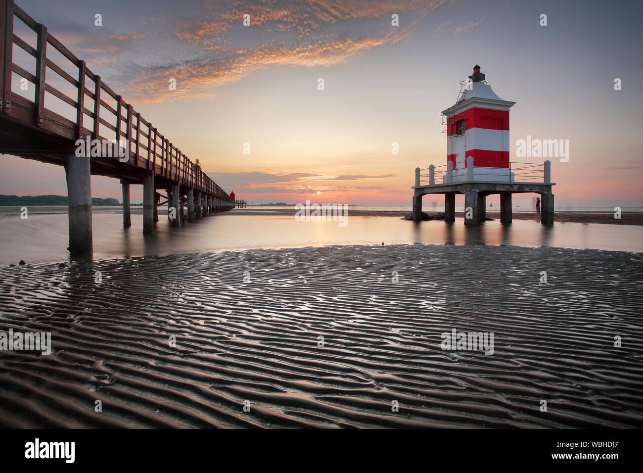 Wooden pier leading to a red lighthouse at sunrise in Lignano Sabbiadoro, Friuli, Italy - beach Stock Photo